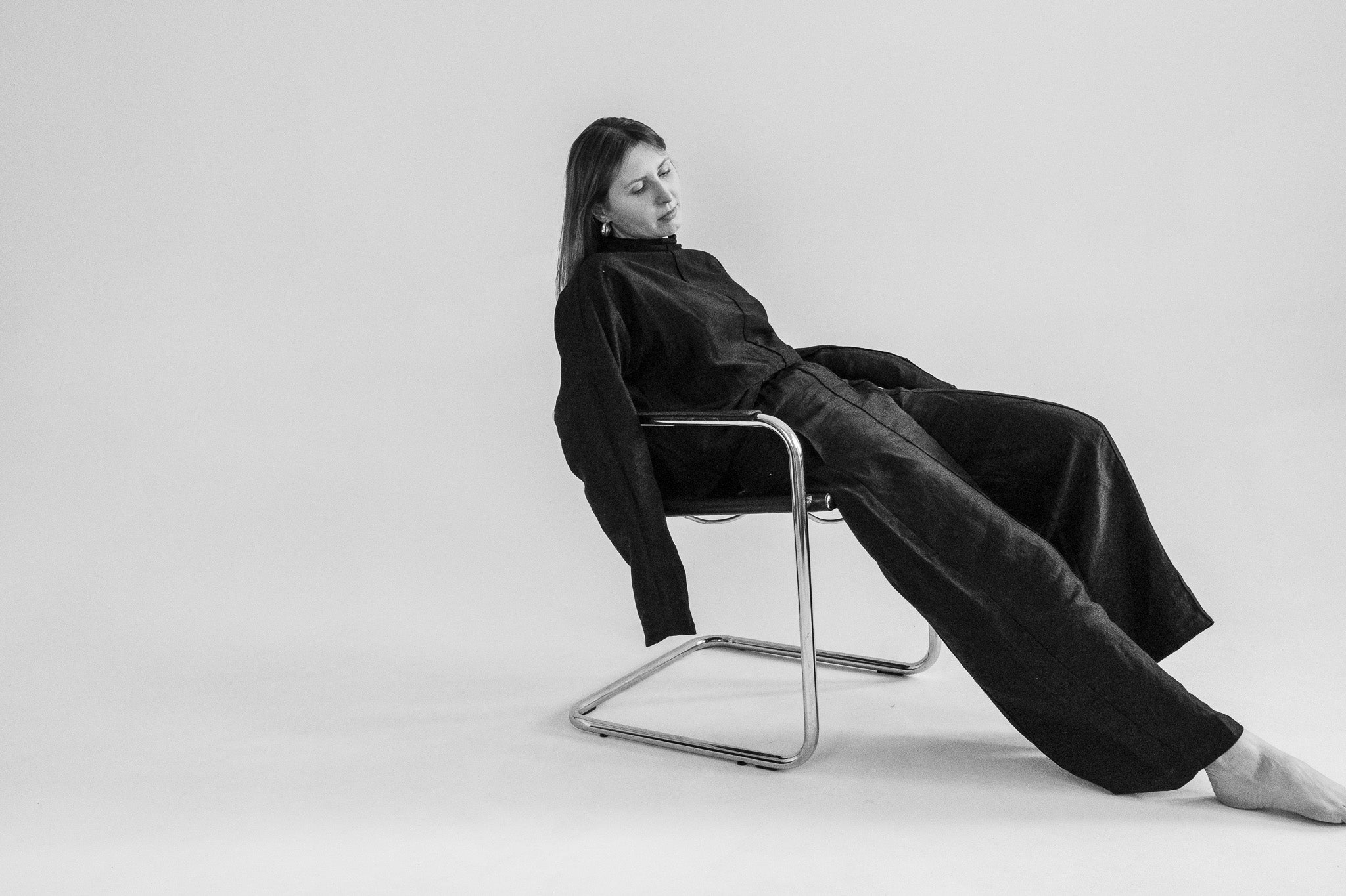 Woman lounging in a minimalist chair wearing ZUBEK’s black silk-linen set. Natural, breathable, and sculpted for elevated low-tox living.