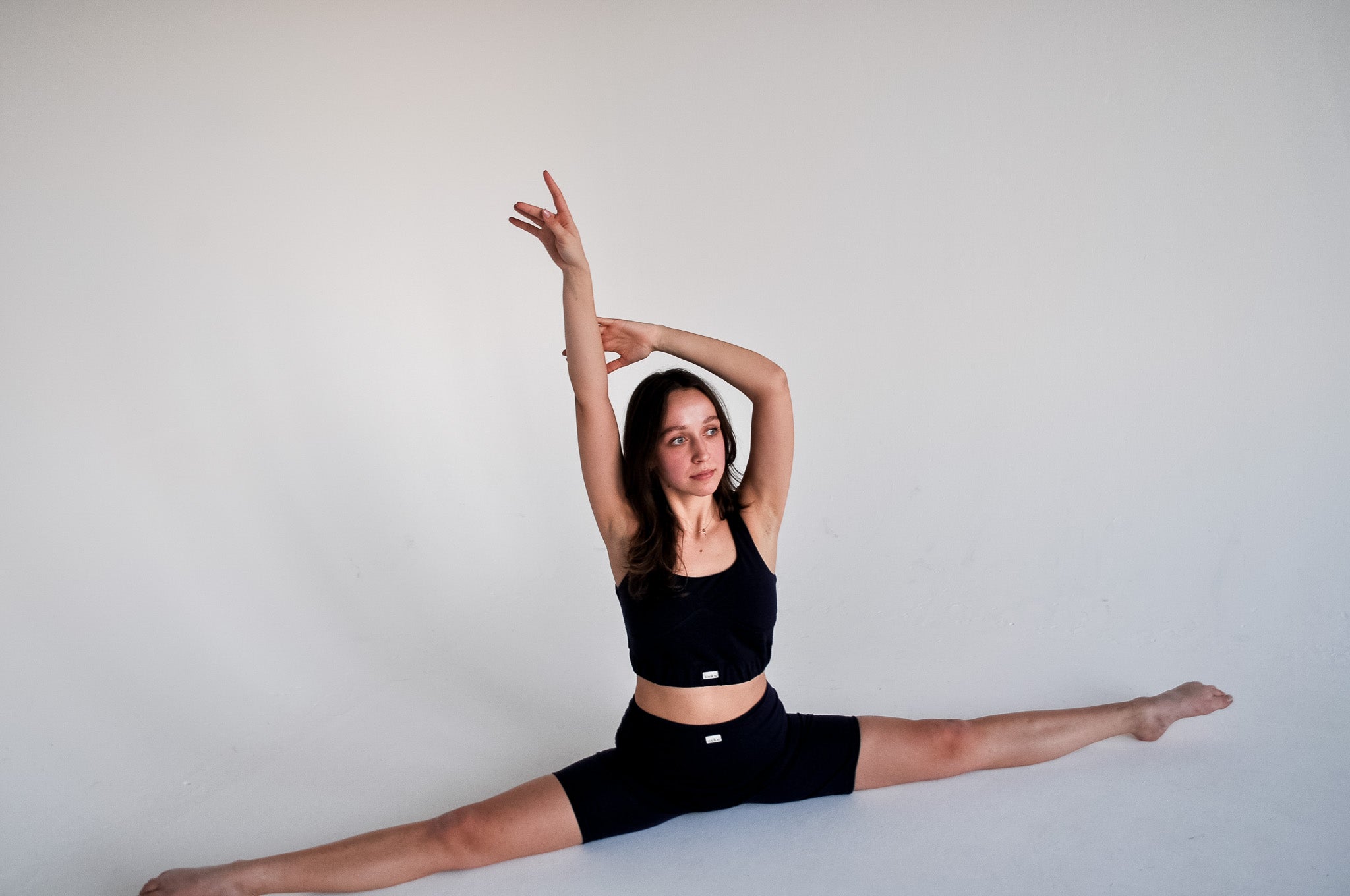 Woman performing a wide seated stretch while wearing ZUBEK's black merino wool sports bra and shorts set. Skin-safe, breathable, and plastic-free activewear.